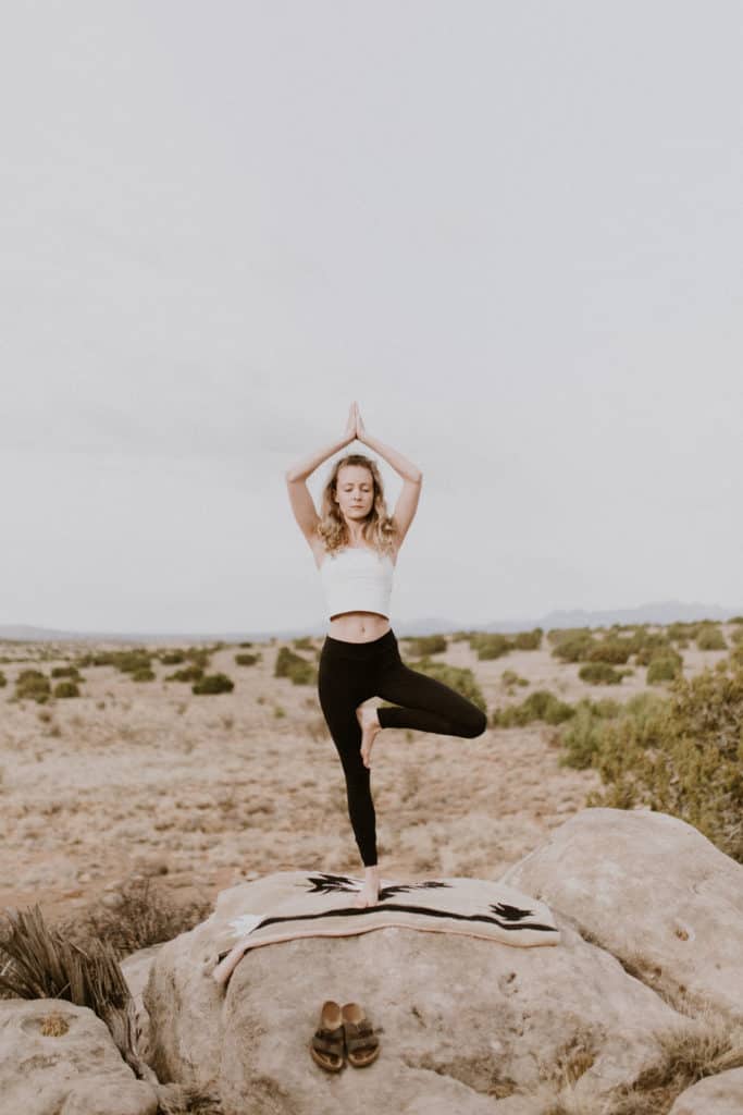 Girl Doing Yoga with Black Leggings on Southwest Style Blanket on Rocks Overlooking Desert Landscape at Glamping Retreat in New Mexico